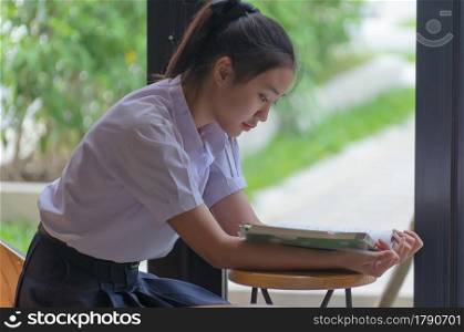 Young Asian college students in uniform beautiful girl relax and smile Read books with relaxed emotions at coffee shop for learning online, Casual business, social meeting, or education concept.. Education concept.