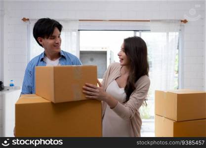 Young Asian couple carrying boxes in their new home. They are standing and smiling.