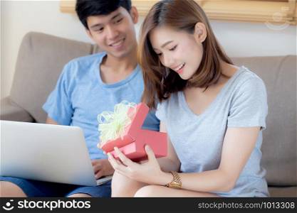 Young asian couple celebrate birthday together, asia man giving gift box present to woman for surprise at living room, female feeling happy and excited anniversary, holiday valentine concept.
