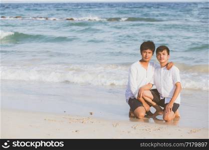 Young asian couple gay smiling romantic drawing word text love together on sand in vacation, homosexual happy and fun with love sitting on sand at the beach in travel summer, LGBT legal concept.