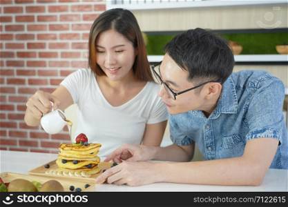 Young asian couple Helping to make a weekend pancake.Asian couples are pouring honey on pancakes.