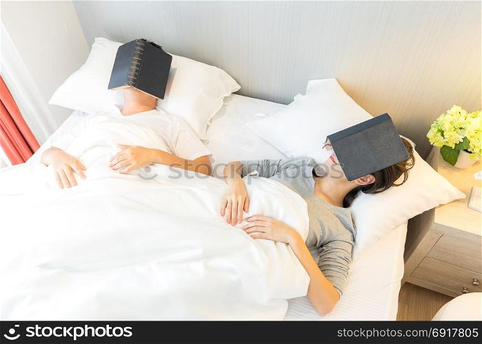 Young Asian Couple laid in a bed reading a book in bedroom of contemporary house for modern lifestyle concept