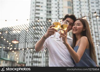Young asian couple lover have fun dancing and drinking in night party on rooftop floor nightclub hand holding beer bottle and eye contact flirting at couple party.focus on two glasses of wine.