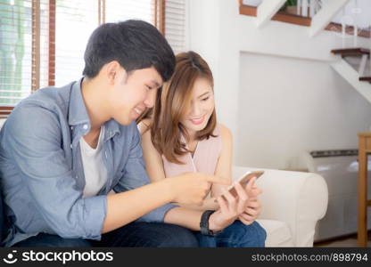 Young asian couple or friend looking smart mobile phone with enjoy at living room, happy family relax and fun media entertainment on smartphone on sofa together at home, lifestyle concept.