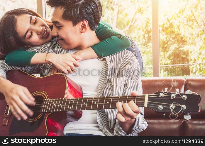Young Asian Couple Plays Guitar and Sing Song in Living Room at Home Together. Music and Lifestyle concept.