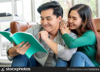 Young Asian couple reading book in living room. Love relationship and lifestyle concept.