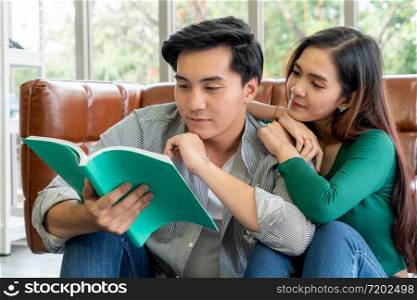 Young Asian couple reading book in living room. Love relationship and lifestyle concept.