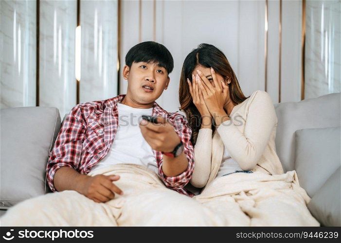Young Asian couple spend time watch scary movie on TV in living room in afternoon, Young man and woman sit on sofa and cover with blanket while watching television together, copy space