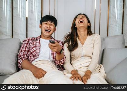 Young  Asian couple watch television on sofa in new house and watch funny movie together. They use remote to change  channel, Happy family Concept