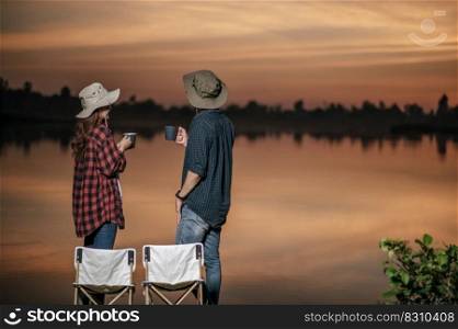 Young Asian couple wearing trekking hat standing and enjoy the beautiful nature on sunset near the lake together during c&ing trip