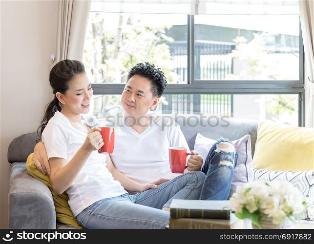 Young Asian Couples drink coffee together in living room of contemporary house for modern lifestyle concept