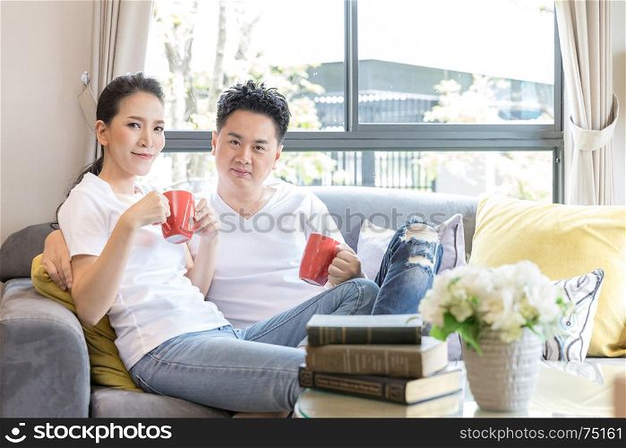 Young Asian Couples drink coffee together in living room of contemporary house for modern lifestyle concept