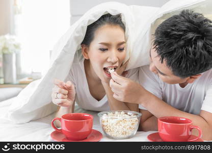 Young Asian Couples having breakfast on bed together in bedroom of contemporary house for modern lifestyle concept