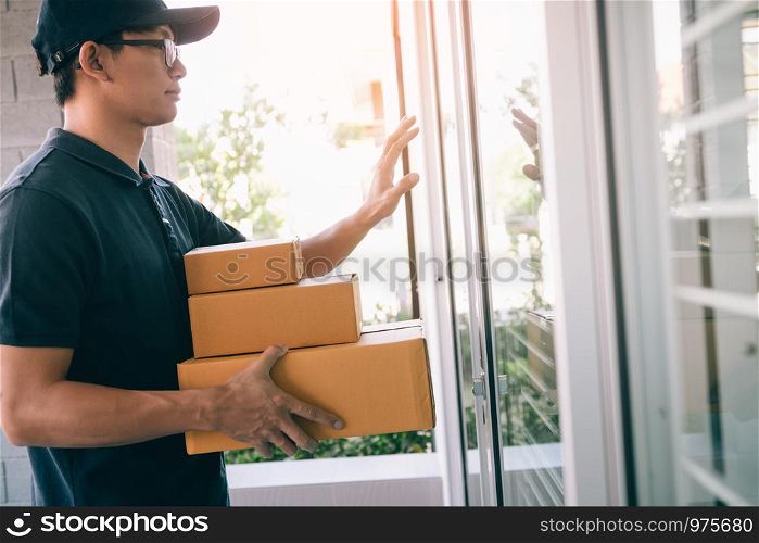 Young asian courier is using the hand of the knock at the door to deliver the goods.