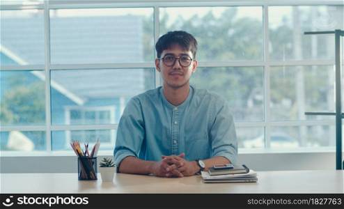 Young Asian creative man smiling in office. Business male happy relax after work, looking to camera, business situation in modern workplace concept.