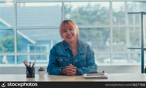 Young Asian creative woman smiling in office. Business female happy relax after work, looking to camera, business situation in modern workplace concept.