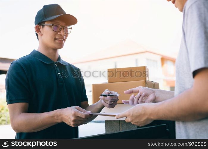 Young asian delivery staff holding the pen and documents submitting giving to the customer receiving the parcel at front house.