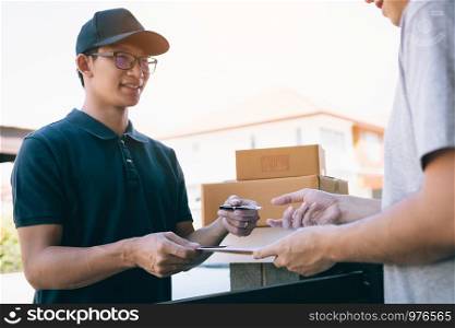 Young asian delivery staff holding the pen and documents submitting giving to the customer receiving the parcel at front house.