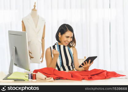 Young Asian Designer woman working and using the technology tablet at workplace over Clothes mannequins, small business startup, Business owner entrepreneur, modern freelance job lifestyle concept