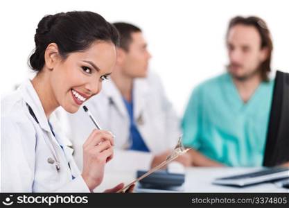 Young asian doctor smiling with the pen and looking the camera, others blurred behind over white background