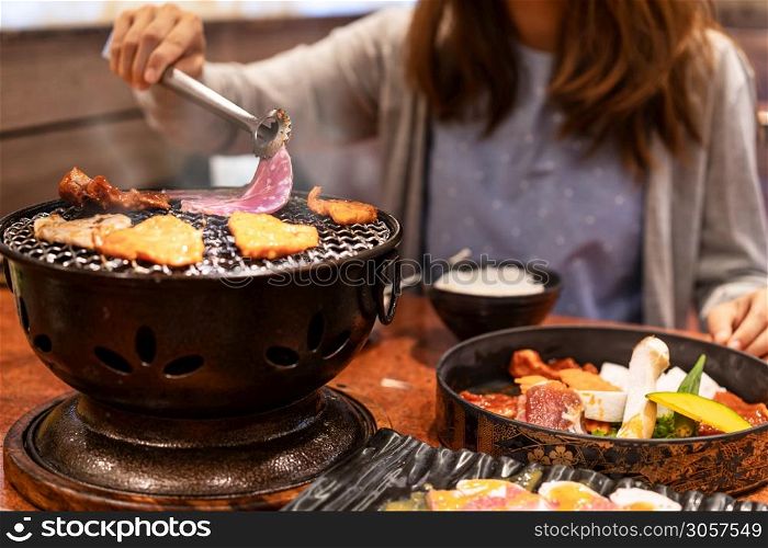 Young asian eating korean barbecue yakiniku in restaurant
