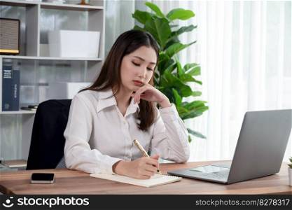 Young asian enthusiastic businesswoman at modern office desk using laptop to work and write notes. Diligent and attractive office lady working on computer notebook in her office work space.. Young asian enthusiastic businesswoman at modern office desk with laptop.