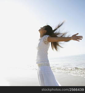 Young Asian female at beach throwing her arms back behind her.