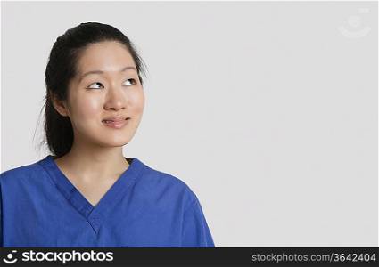 Young Asian female doctor looking up over gray background