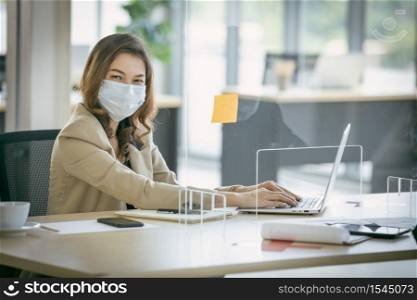 Young asian female entrepreneur wearing face mask while working on laptop in the office.