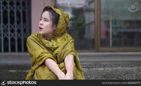 young asian female in yellow hoody rain coat sit down waiting on the street side on the rainy day, stuck in the rain, self protection from, wet clothes stuck in the rain, wait for rain to stop