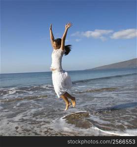 Young Asian female jumping in air at the shoreline.