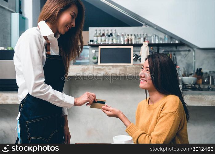 Young Asian female make a payment to coffee shop owner by credit card with a background of beverage bar counter in small coffee shop. Young Woman pay for her coffee with credit card. Food and drink.