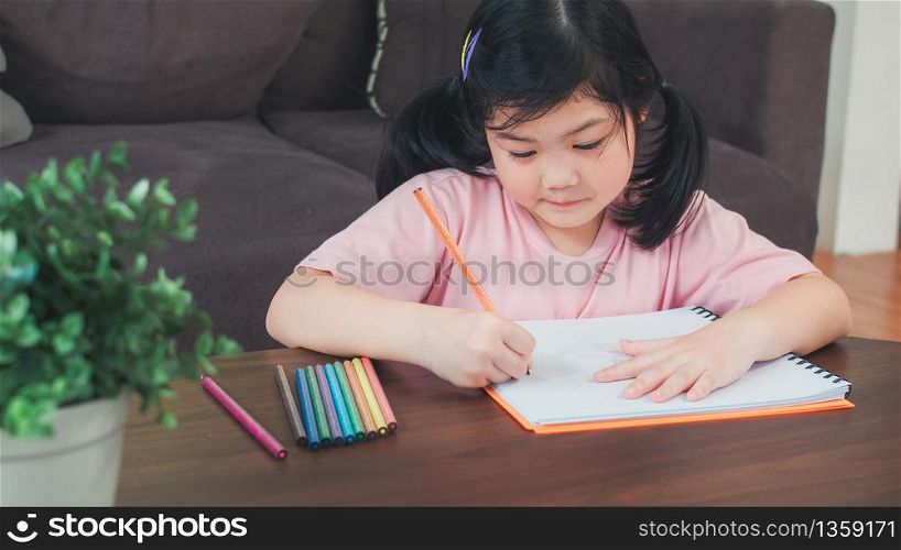 Young Asian girl drawing at home. Asia japanese woman child kid relax rest fun happy draw cartoon in sketchbook lying on sofa, feel comfort and calm in living room in the morning concept.