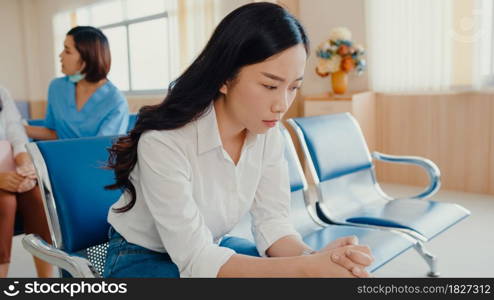 Young Asian girl sitting on chair waiting room feel scary for bad news stress hopeless and sadness for her father in front surgical room at hospital, Hospital environment concept.