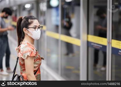 young Asian girl wearing Surgical face mask protect coronavirus inflection, Happy tourist woman wating public train. social distancing, new normal and life after covid-19 pandemic