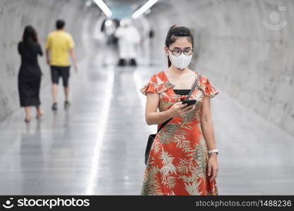 young Asian girl wearing Surgical face mask protect coronavirus inflection, Happy tourist woman using smartphone during walking in subway station. new normal and life after covid-19 pandemic