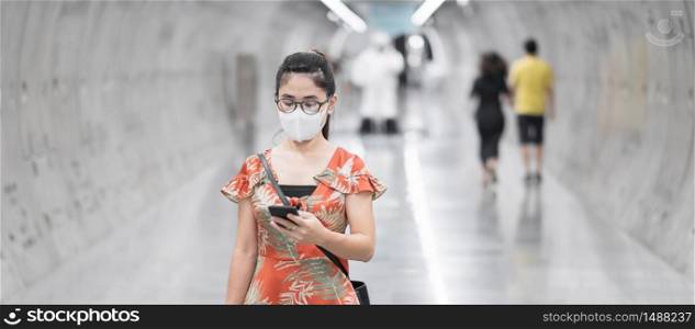young Asian girl wearing Surgical face mask protect coronavirus inflection, Happy tourist woman using smartphone during walking in subway station. new normal and life after covid-19 pandemic