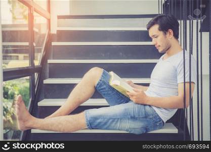 Young asian handsome man reading book for relax at home, male activities for leisure, education success concept.