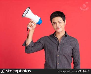 Young asian handsome man screaming with megaphone on red background in studio shot.