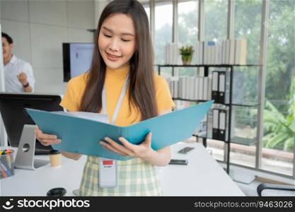 Young Asian Happy Businesswoman or intern holding documents in Modern Office background is Colleagues discuss with new startup project Idea. Empowered Digital Entrepreneur Works on Startup Project