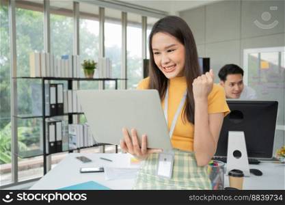 Young Asian Happy Businesswoman or intern using Computer in Modern Office background is Colleagues discuss with new startup project Idea. Empowered Digital Entrepreneur Works on Startup Project