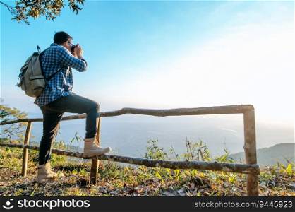 Young Asian hiker man and backpack use camera to take pictures on view point in forest. copy space