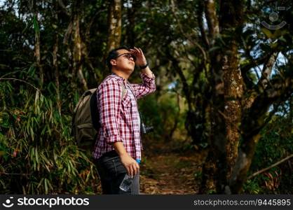 Young Asian hiker man with backpack and camera walking on trail in nature forest. copy space