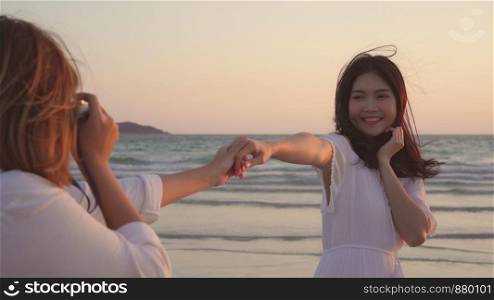 Young Asian lesbian couple using camera taking photo each other near beach. Beautiful women lgbt couple happy romantic moment when sunset in evening. Lifestyle lesbian couple travel on beach concept.