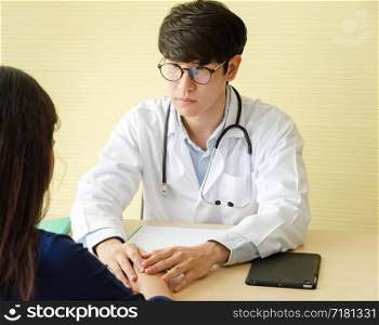 Young asian male doctor with glasses talking and holding female patient hand for encouragement and empathy bad news of medical examination. Healthcare and medical concept