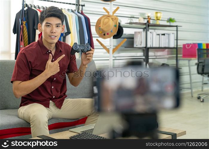 Young asian male online blogger recording live vlog video for review joystick for gaming IT product goods. Online influcencer on social media concept. Focus on mobile phone