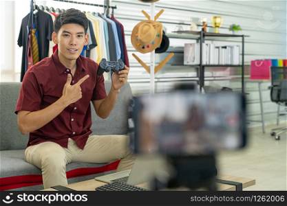 Young asian male online blogger recording live vlog video for review joystick for gaming IT product goods. Online influcencer on social media concept. Focus on mobile phone