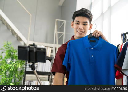 Young asian male online merchant fashion blogger using smart mobile phone to recording live vlog video for review casual wear clothes. Online influcencer on social media concept.