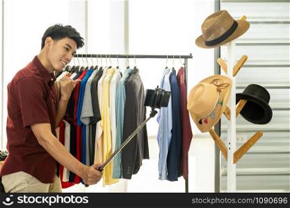Young asian male online merchant fashion blogger using smart mobile phone to recording live vlog video for review casual wear clothes. Online influcencer on social media concept.