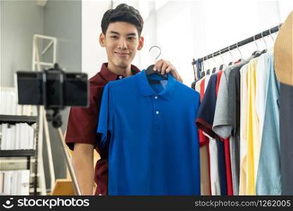 Young asian male online merchant fashion blogger using smart mobile phone to recording live vlog video for review casual wear clothes. Online Influencer on social media concept.